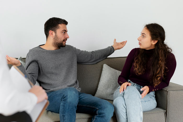 Dad and mom discuss kids&rsquo; aggressive MMA classes on a gray sofa.