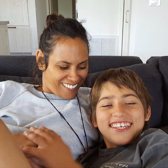 A woman and a boy smiling and relaxing on a couch, showcasing a warm and joyful moment, related to Colin Farrell's parenting.