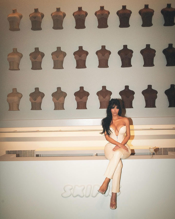 Woman in cream outfit posing amid mannequin wall display.