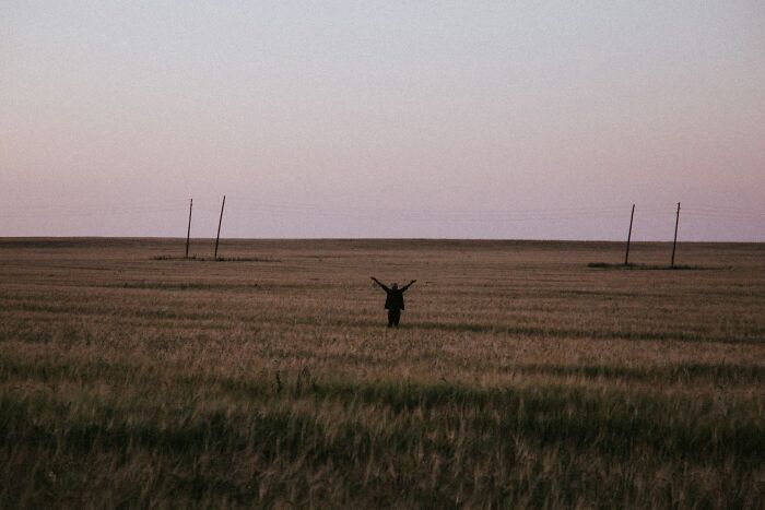 Person standing with arms raised in a vast field at dusk, symbolizing first responders remembering a life-changing call.