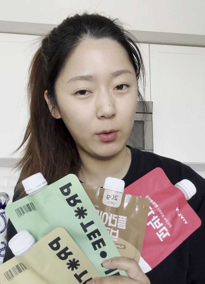 Young woman holding Switch-On Diet pouches, promoting fat shedding and muscle maintenance results in a kitchen setting.