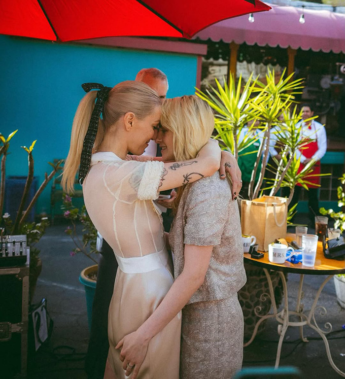 Lovebirds embrace at an outdoor wedding, sharing an intimate moment under a red umbrella.