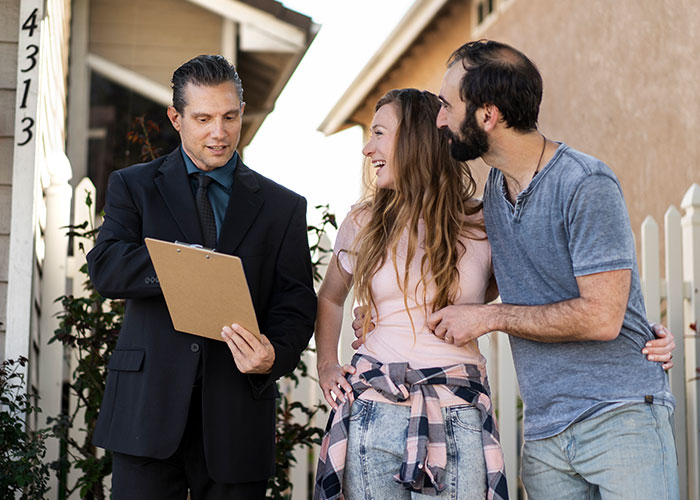 Man with clipboard talking to a smiling couple outside their home, discussing landlord matters. Man with clipboard talking to a smiling couple outside their home, discussing landlord matters.