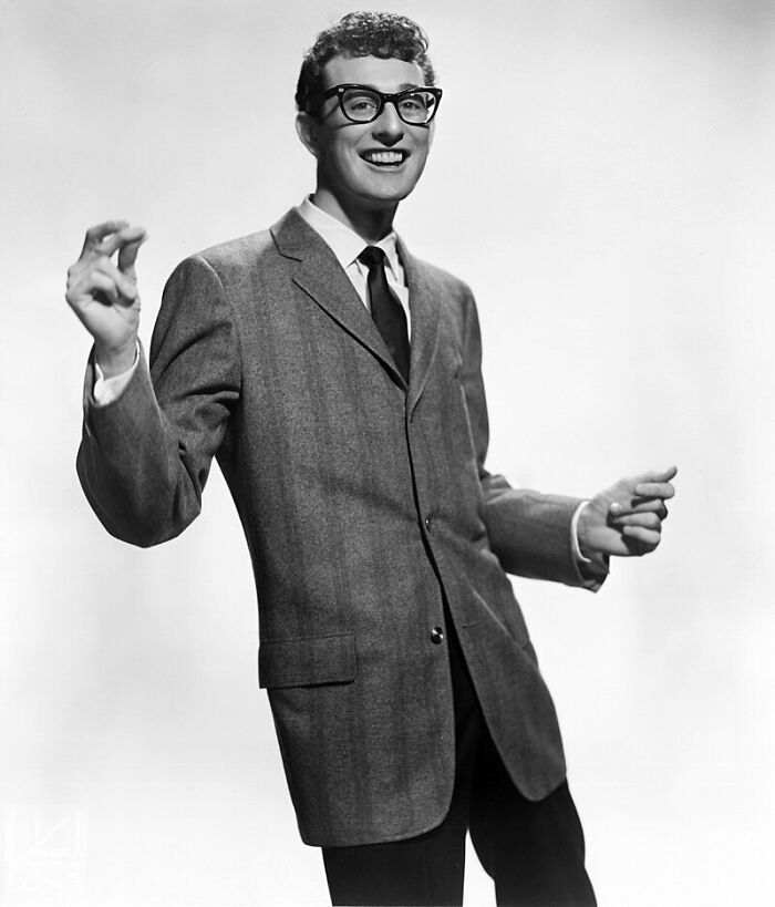 Young man in glasses wearing a suit jacket, smiling and gesturing, illustrating last-minute decisions that changed history.