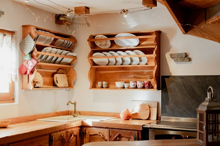 Rustic kitchen with open wooden shelves displaying dishes, showing vessel sinks and cozy, impractical aesthetics.