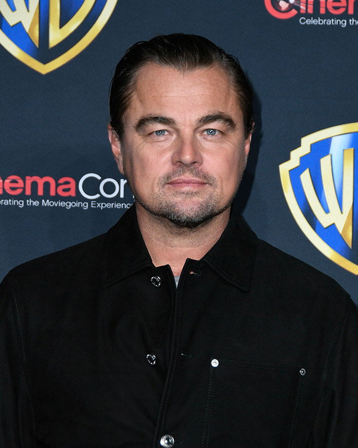 Man in a black jacket at a red carpet event in front of a branded backdrop, showcasing a midlife change.