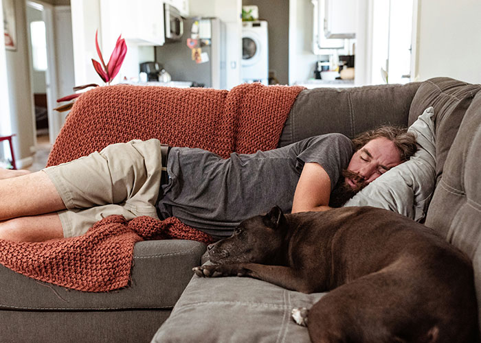 Man napping on sofa with dog, illustrating lifestyle choices that scream "red flag".