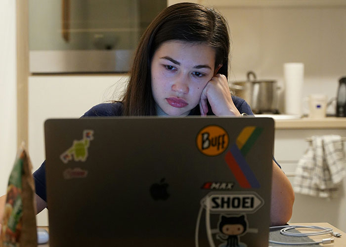 Woman looking stressed while working on a laptop in a kitchen, illustrating a lifestyle choice red flag.