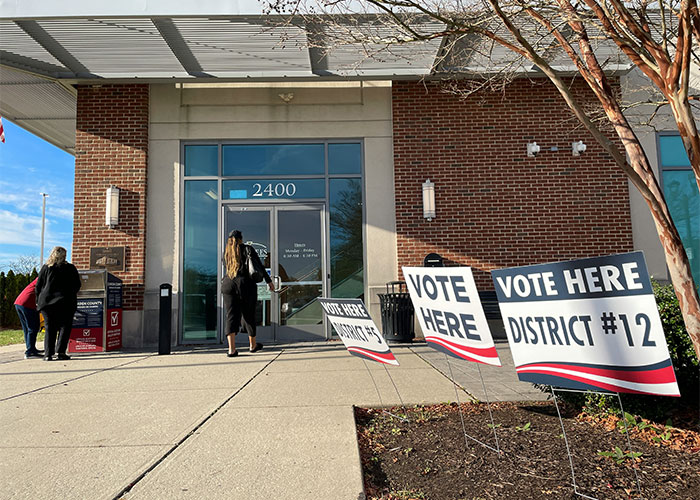 People entering a voting location, with "Vote Here District #12" signs outside, highlighting potential lifestyle red flags.