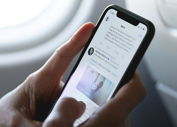 Person scrolling through Twitter on a smartphone, focusing on tweets.