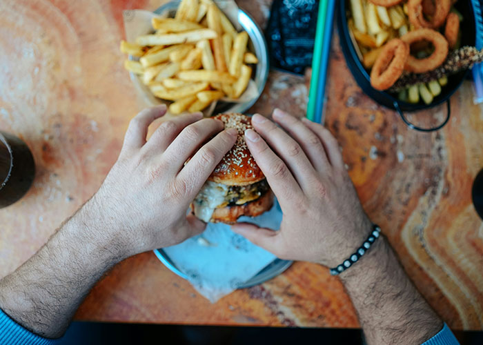 Hands holding a burger with fries, displaying lifestyle red flags through unhealthy eating habits.