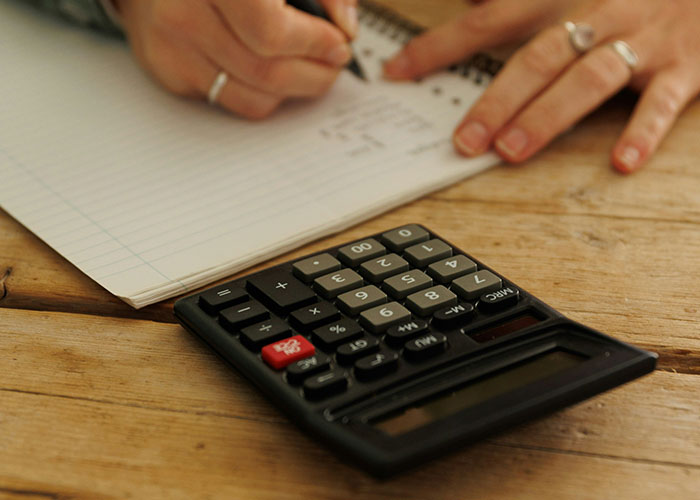 Person writing calculations in a notebook with a calculator nearby, illustrating lifestyle choices.