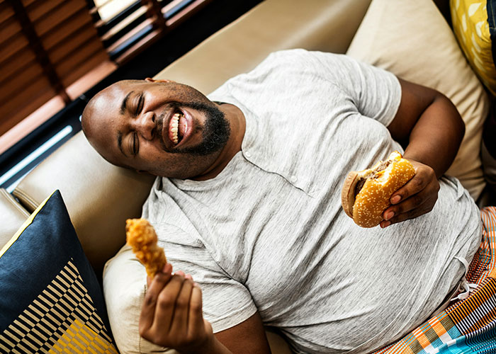 Man laughing on a couch with fast food, highlighting lifestyle red flags.