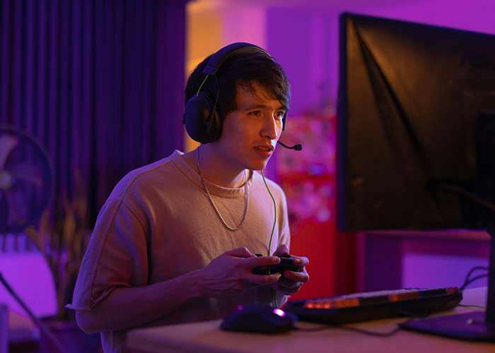Person gaming intensely with headphones in a dimly lit room, highlighting lifestyle choices.