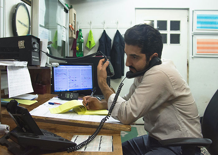 Man multitasking with phones at a cluttered desk, writing notes, symbolizing lifestyle red flags.