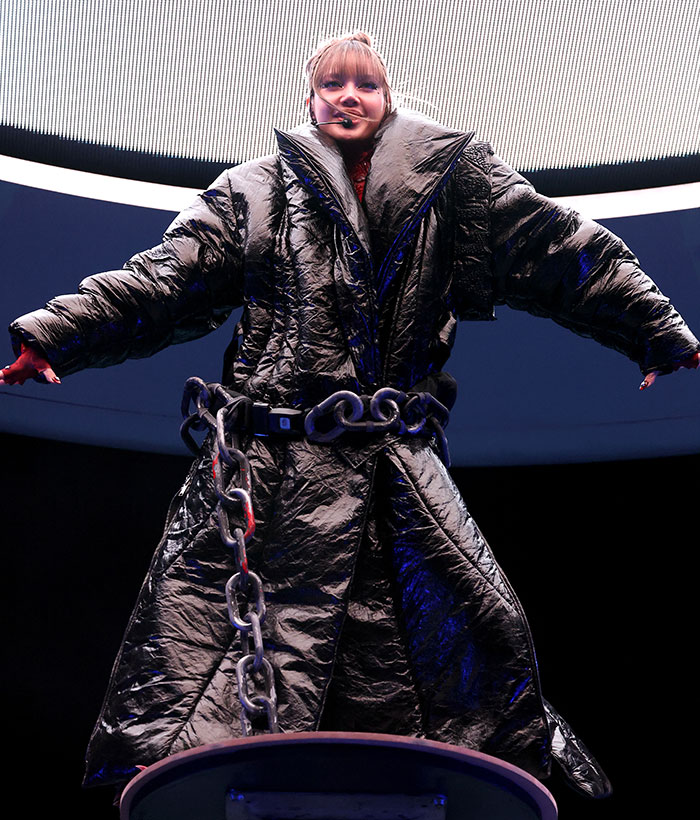 Celebrity in an oversized metallic coat with chain belt at Coachella 2025, showcasing a bold and unconventional fashion choice.