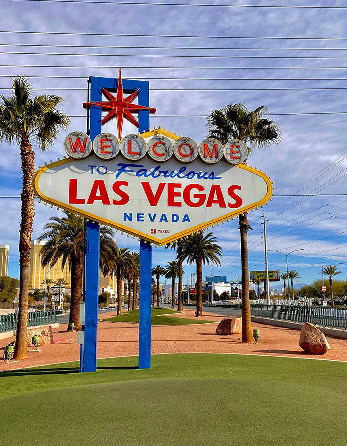 Welcome sign to Las Vegas under a blue sky, surrounded by palm trees, highlighting the city's iconic entrance.