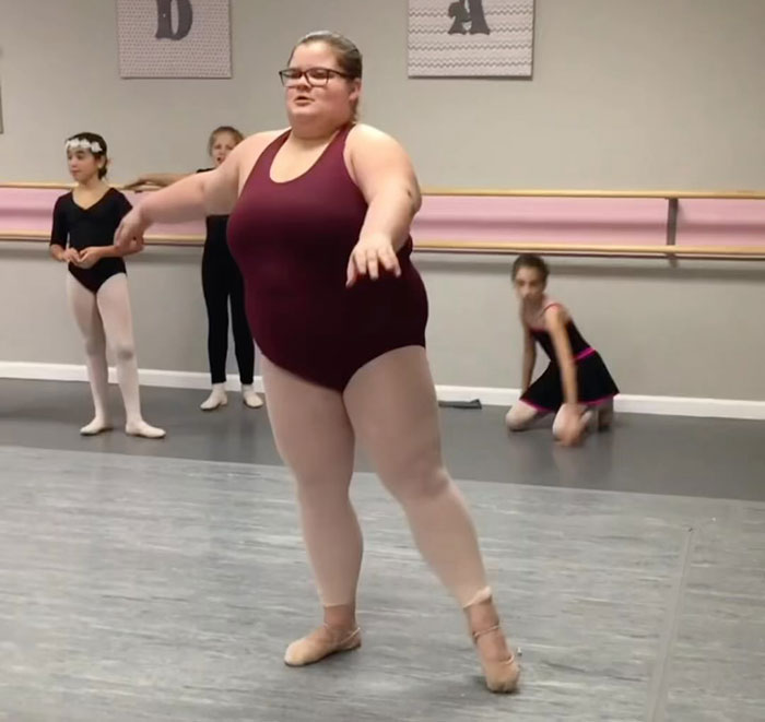 Plus-size dancer in maroon leotard performing in ballet class, highlighting diversity in dance.