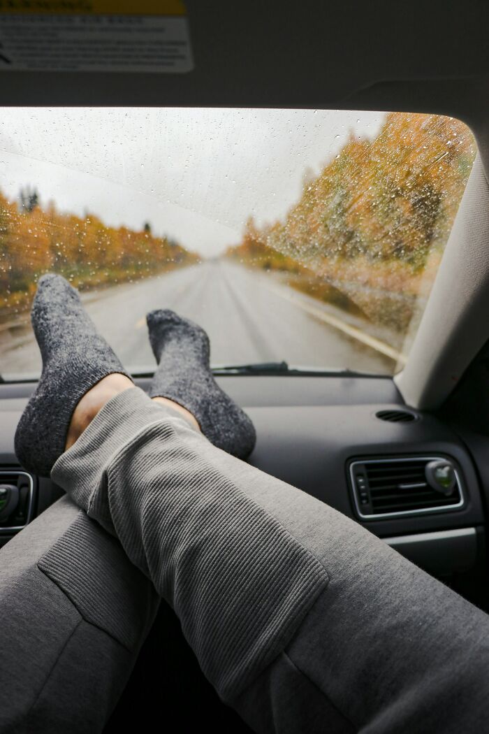 Person wearing gray sweatpants and dark socks resting feet on car dashboard with rainy autumn road ahead, first responders theme