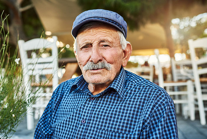 Elderly man with mustache wearing a blue cap and checkered shirt, representing long-lost grandfather and inheritance theme.