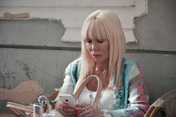 Middle-aged woman with blonde hair checking phone, focused on looking up long-lost grandfather for inheritance.