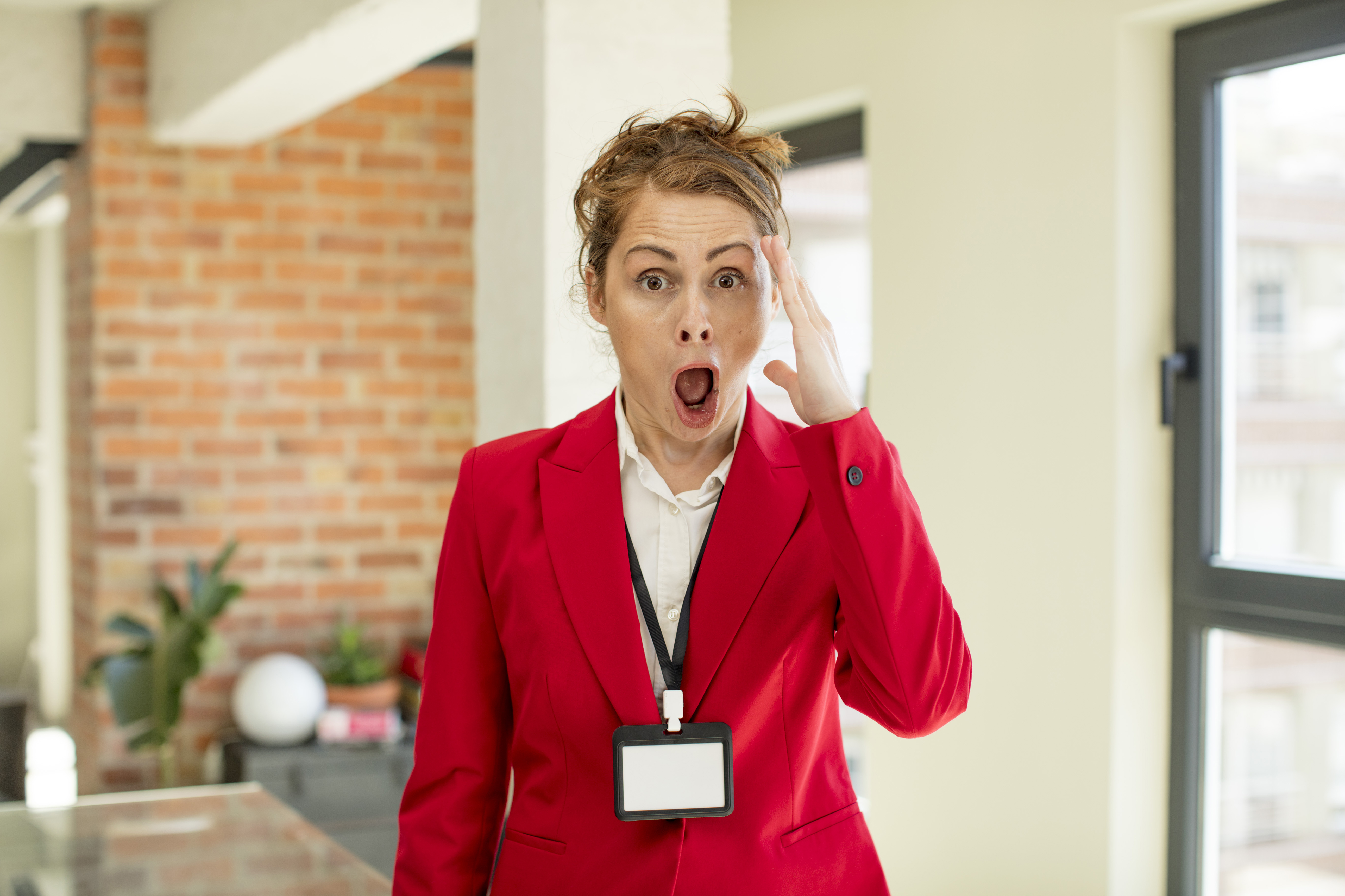 Event manager in a red suit looking shocked with hand on forehead indoors.