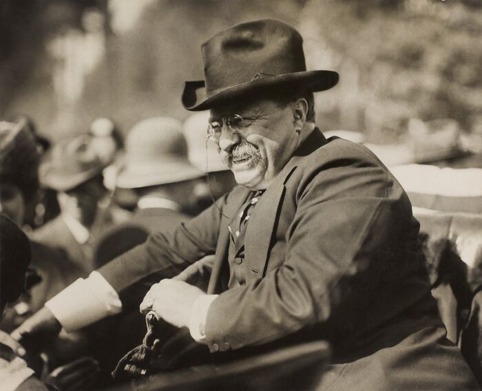 Rare photo of a famous historical figure wearing a suit and hat, smiling outdoors among a crowd of people.