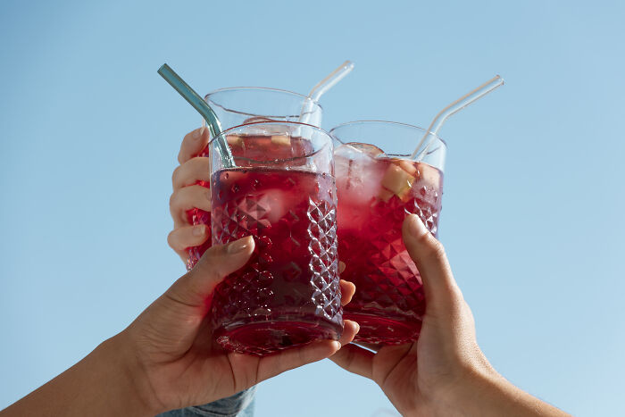 Hands raising glasses of red drinks with ice against a clear sky; a curious European beverage moment.