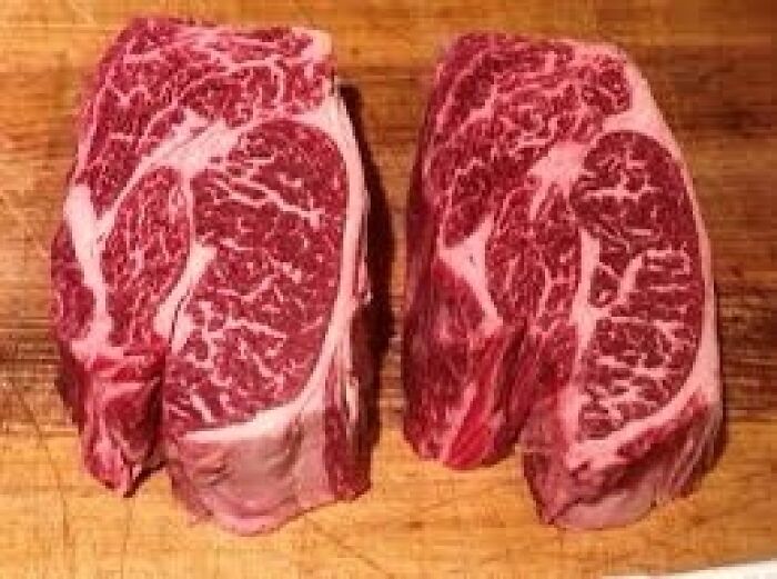 Two marbled raw steaks on a wooden surface, showcasing quality homemade food.