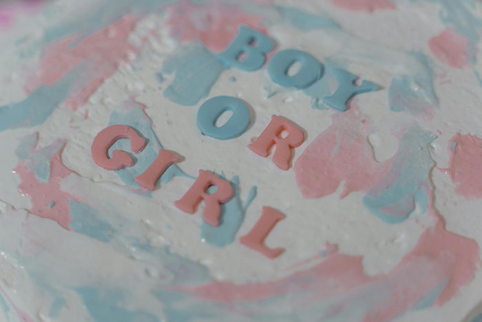 Close-up of a gender reveal cake with pink and blue icing spelling out boy or girl predicting pregnant friend&rsquo;s baby gender.