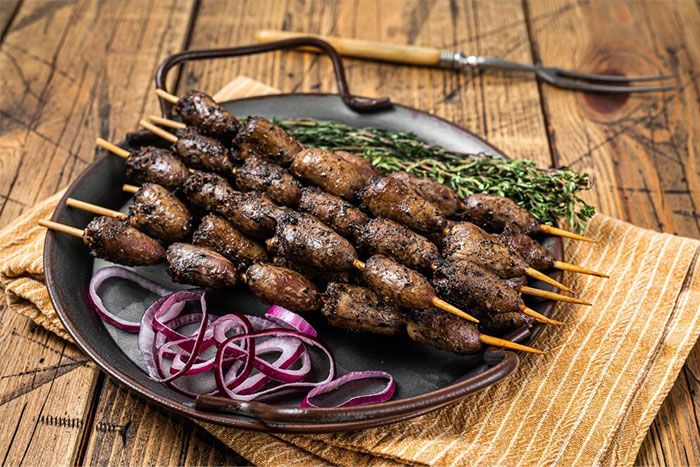 Skewers of cultural food on a plate with herbs and sliced onions.