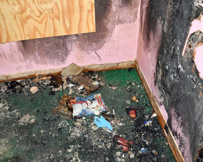 Damaged room showing evidence of long-term captivity, with debris and burned items on the floor.