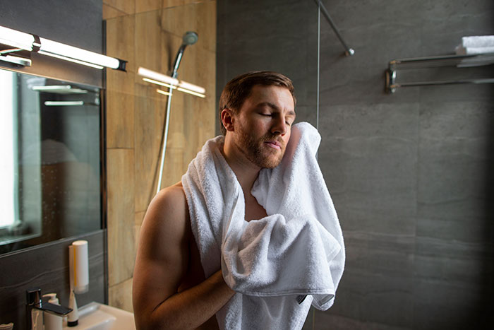 Man in bathroom drying face with towel, reflecting on lessons about being present learned from his partner.