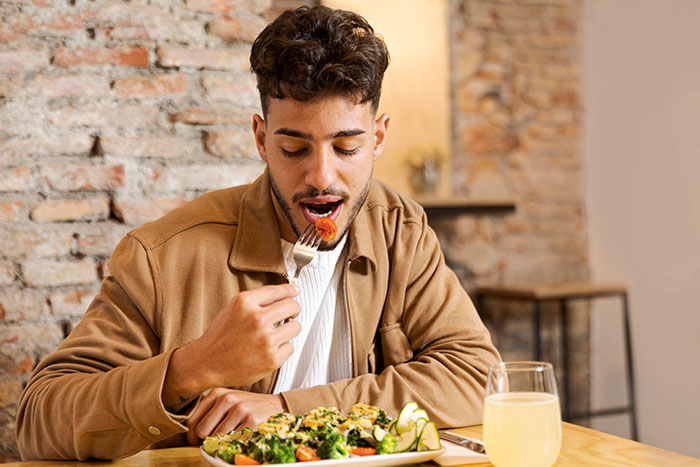 Young man practicing being present while eating a healthy meal in a cozy restaurant with exposed brick walls.