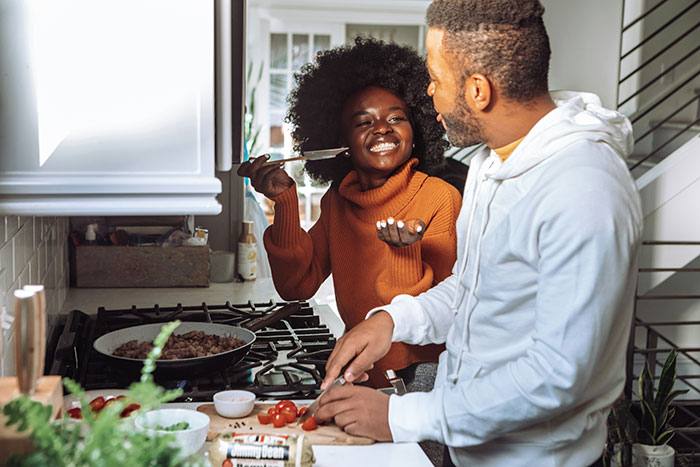 Couple cooking together in a bright kitchen, sharing a joyful moment focused on being present and connecting.