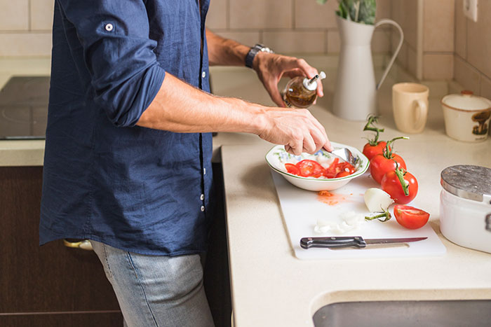 Man preparing tomatoes in the kitchen, demonstrating the importance of being present while cooking and engaging in daily tasks.