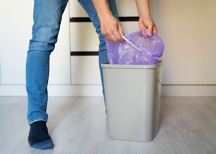 Man placing a purple trash bag into a bin, demonstrating being present and mindful in everyday household tasks