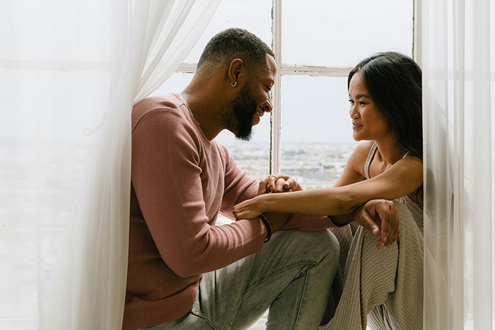 Couple sitting by a window, sharing a moment of connection and mindfulness, illustrating being present in relationships.