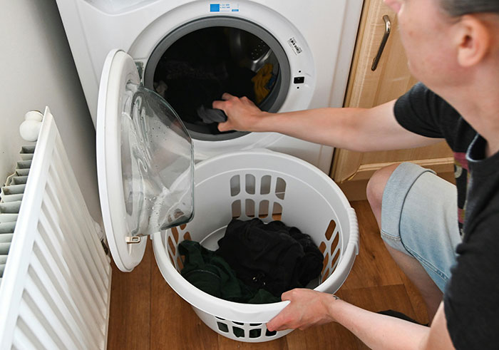 Man loading clothes into a washing machine, illustrating practical habits learned from partners to be present in everyday tasks.