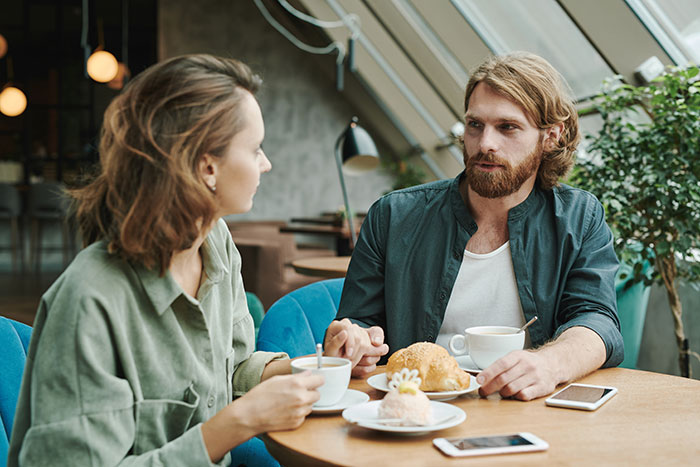 A couple having coffee and pastries at a cafe, engaging in a meaningful conversation about being present in relationships.