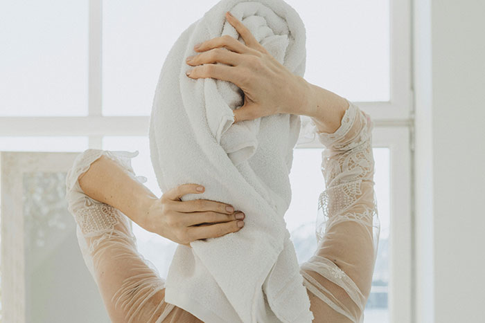 Woman wrapping a towel around her hair in a bright room, symbolizing the lesson to be present and mindful.