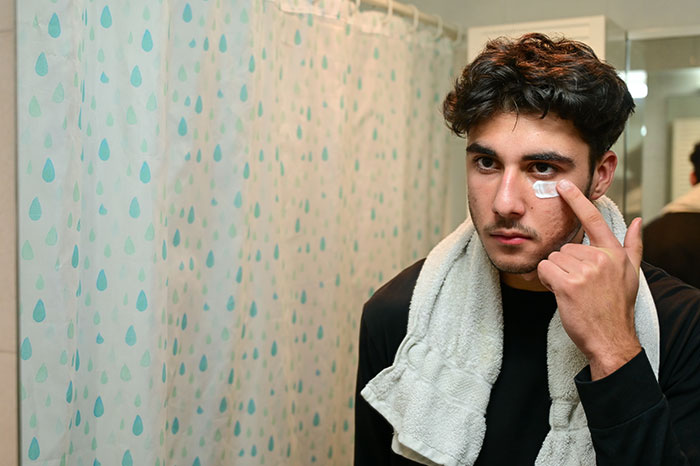 Young man applying skincare cream in bathroom mirror, focusing on self-care and being present habits learned from partners