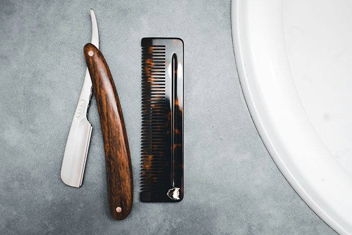 Straight razor and comb on a bathroom counter symbolizing grooming habits men learned from their partners to be present.