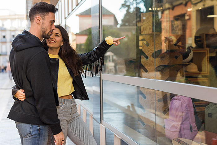 Couple shopping together, woman pointing at items in store window, illustrating lessons men learned from partners.