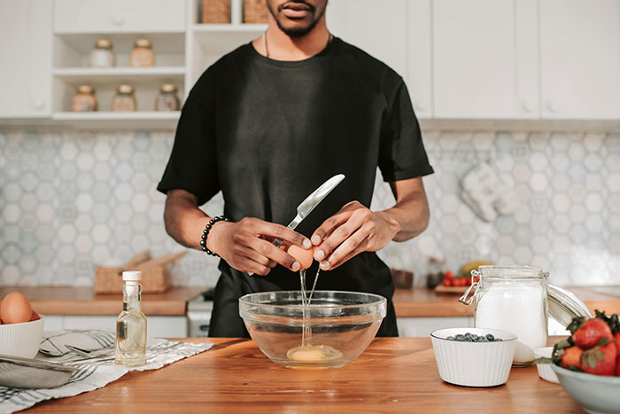 Man practicing being present while cracking an egg into a bowl in a well-lit kitchen setting.