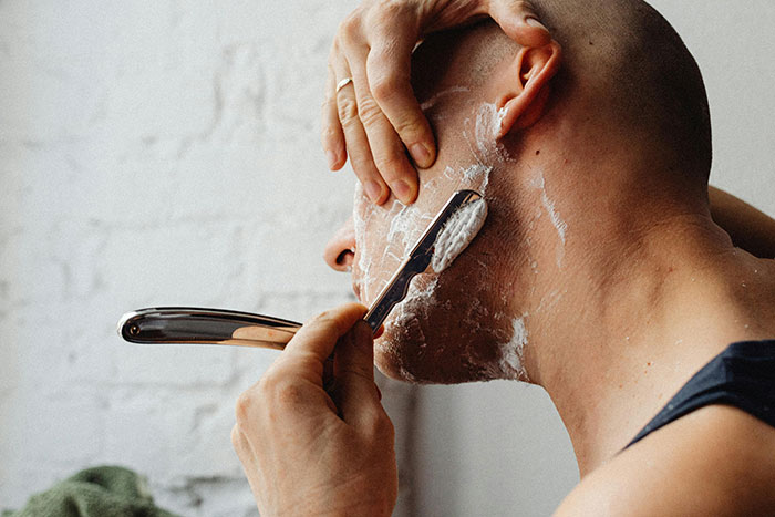 Man shaving carefully using a straight razor, focusing on being present and mindful during his grooming routine.