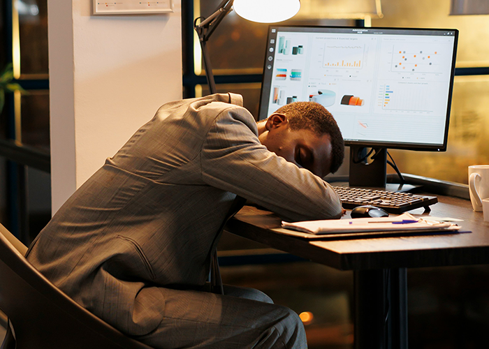 Employee exhausted at desk with computer displaying charts, reflecting lack of team player sentiment. Employee exhausted at desk with computer displaying charts, reflecting lack of team player sentiment.