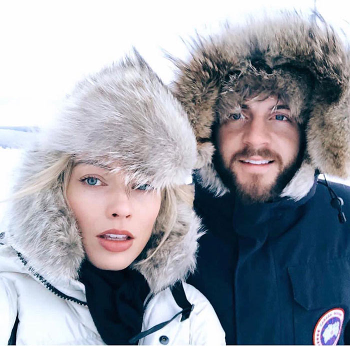 Two people in winter coats with fur hoods in a snowy setting, showcasing a natural postpartum look.