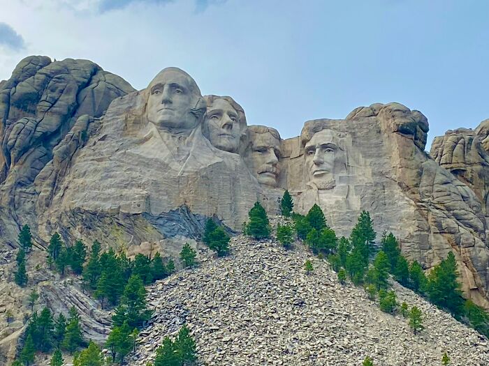 Mount Rushmore, a famous tourist attraction, viewed against a blue sky with surrounding greenery.