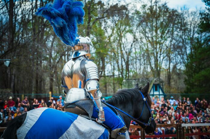 Knight in shiny armor on horseback at a jousting event, exuding absolute confidence amidst a large crowd.